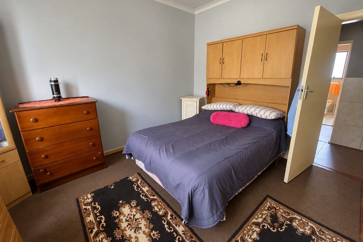 A functional bedroom featuring built-in wooden cupboards, carpeted flooring, and neutral wall finishes, offering a practical layout for a comfortable sleeping space.