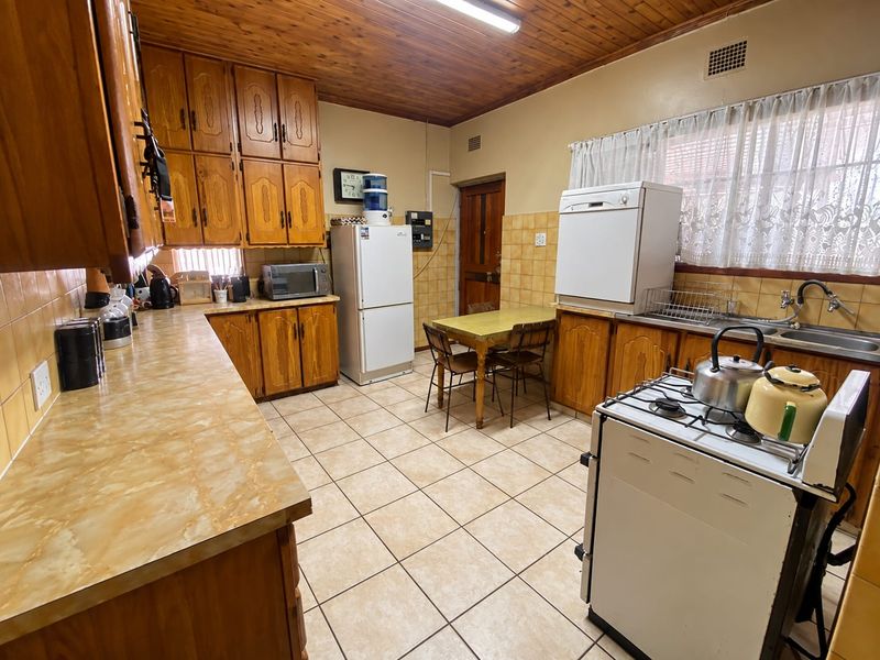 A functional kitchen featuring traditional wooden cabinetry, laminate countertops, tiled flooring, and a classic wooden ceiling, offering a dated but well-maintained layout.