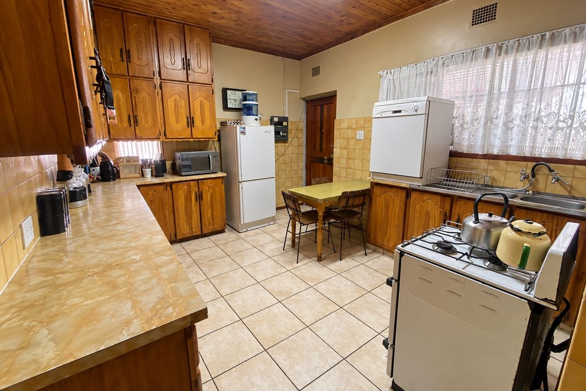 A functional kitchen featuring traditional wooden cabinetry, laminate countertops, tiled flooring, and a classic wooden ceiling, offering a dated but well-maintained layout.