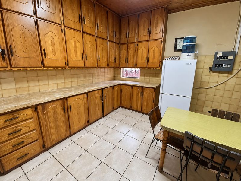 A functional kitchen featuring extensive timber cabinetry, laminate countertops, tiled splashbacks, and tiled flooring, offering significant potential for a modern renovation.