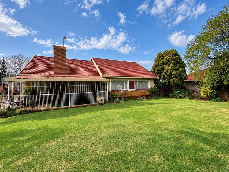 Rear view of the house featuring a tiled roof, brick chimney, and a covered patio area overlooking a spacious lawn.