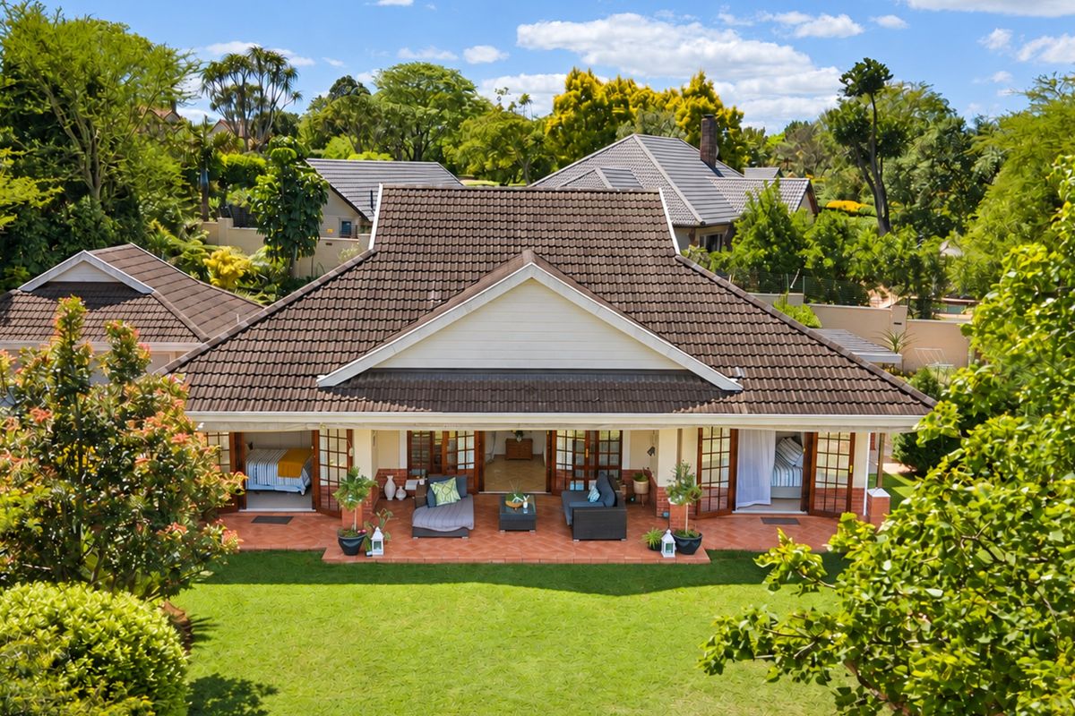 Aerial view of the rear elevation featuring a spacious terracotta patio, multiple sets of french doors, and a well-maintained garden.