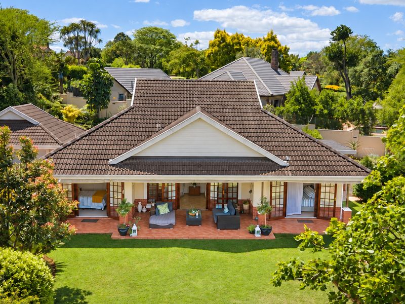 Aerial view of the rear elevation featuring a spacious terracotta patio, multiple sets of french doors, and a well-maintained garden.
