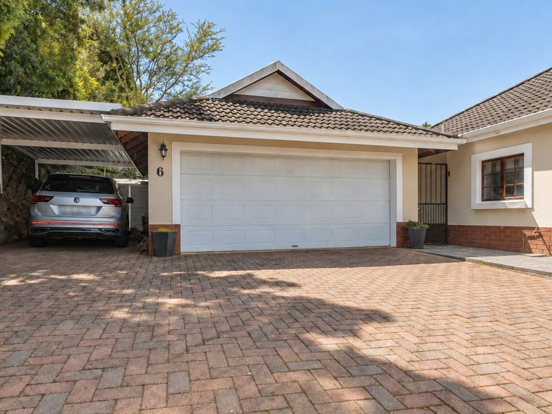 Front exterior view of a townhouse featuring a double garage, attached carport, and a spacious paved driveway.