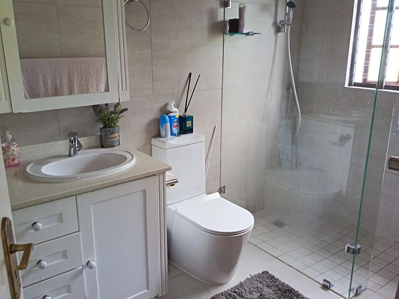 A well-maintained bathroom featuring a white vanity cabinet, integrated basin, wall-mounted medicine cabinet, and a modern glass-enclosed shower with rainfall shower head.