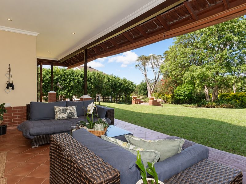 A spacious covered patio featuring tiled flooring and timber roof beams, offering seamless indoor-outdoor flow to a well-maintained private garden.