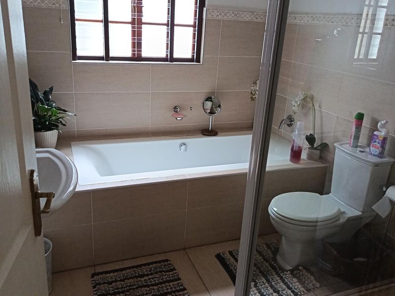 A functional bathroom featuring a built-in bathtub, a separate glass-enclosed shower, and neutral wall tiling with a window for natural light.