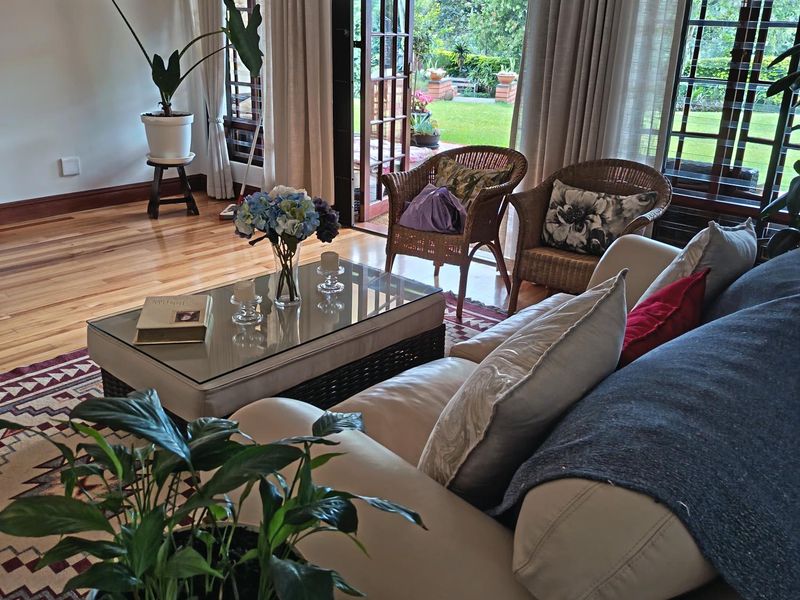 A bright living room featuring polished hardwood flooring and large timber-framed glass doors that provide seamless access to the outdoor garden area.