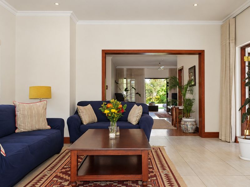 Spacious living room featuring neutral tiled floors, crown molding, recessed lighting, and a wide wooden-framed opening leading to an adjacent living area.