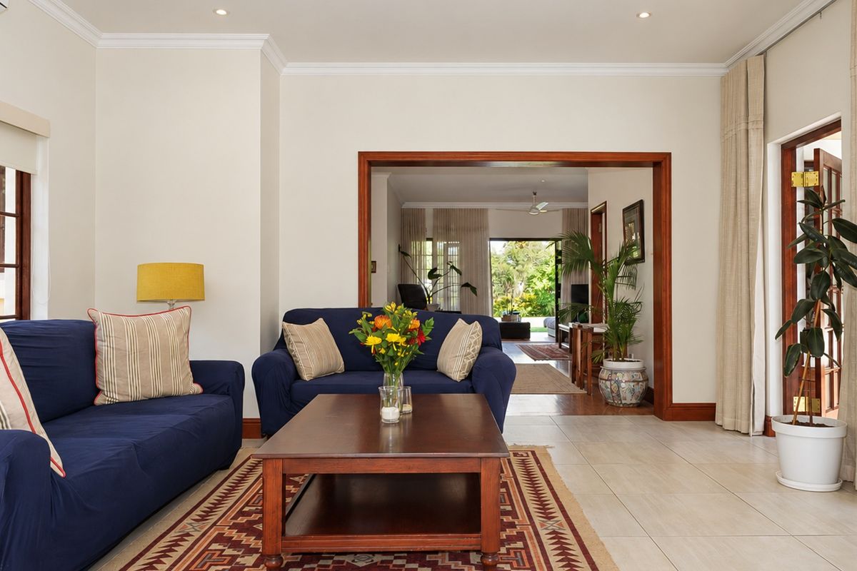 Spacious living room featuring neutral tiled floors, crown molding, recessed lighting, and a wide wooden-framed opening leading to an adjacent living area.