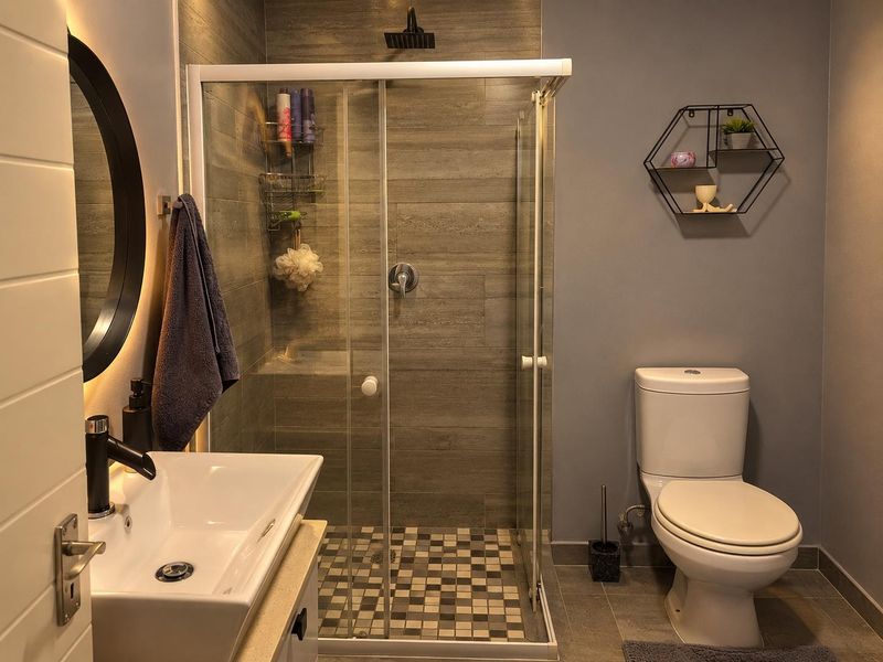 Modern bathroom featuring a glass-enclosed shower with rain shower head, wall-mounted basin, and contemporary tiled finishes.