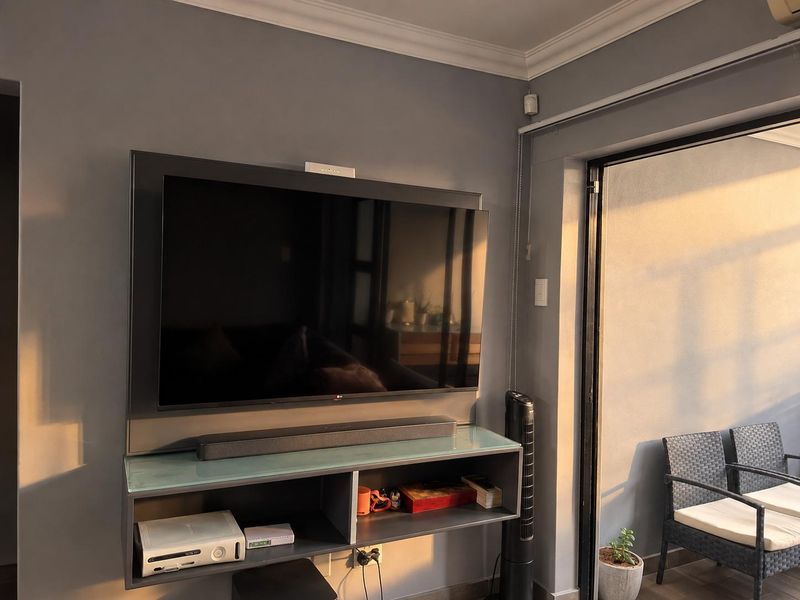 A living room area featuring a wall-mounted television, built-in shelving, and access to an outdoor balcony through a sliding glass door.