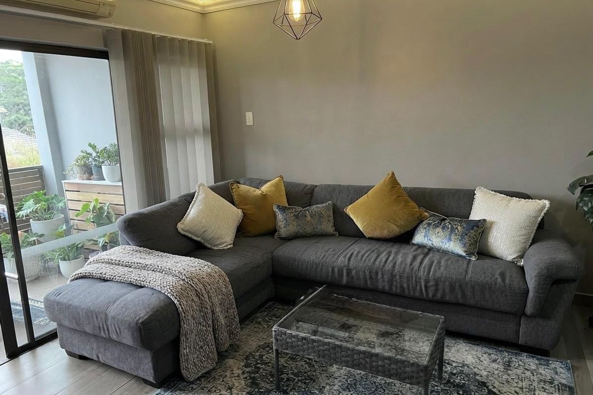 A well-maintained living room featuring modern recessed ceiling lighting, laminate flooring, and a large sliding glass door providing access to a balcony.