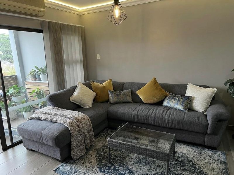 A well-maintained living room featuring modern recessed ceiling lighting, laminate flooring, and a large sliding glass door providing access to a balcony.