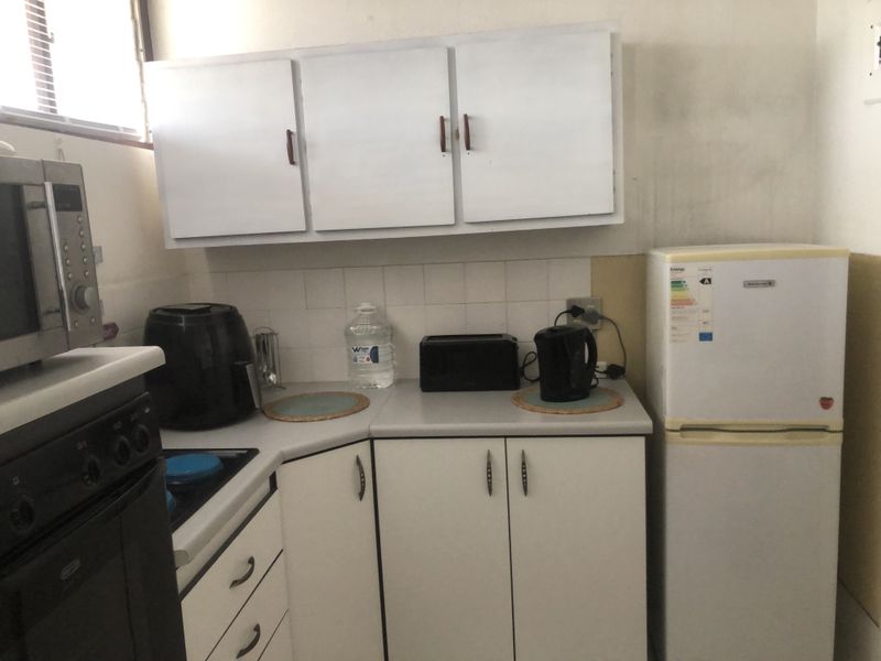 Compact kitchen featuring white cabinetry, tiled backsplash, and built-in cooking appliances. The space would benefit from cosmetic updates to finishes and wall surfaces.