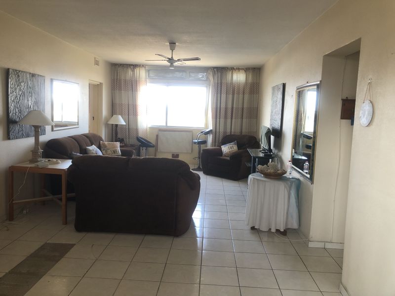 A spacious living room featuring tiled flooring, a ceiling fan, and large windows that provide natural light.