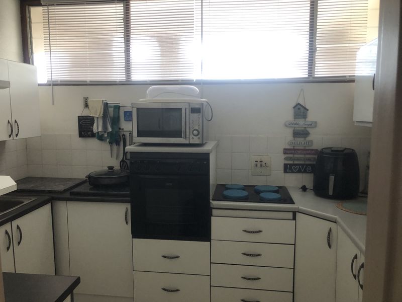 A functional kitchen featuring white cabinetry, dark laminate countertops, a built-in oven, electric hob, and tiled splashback with large windows.