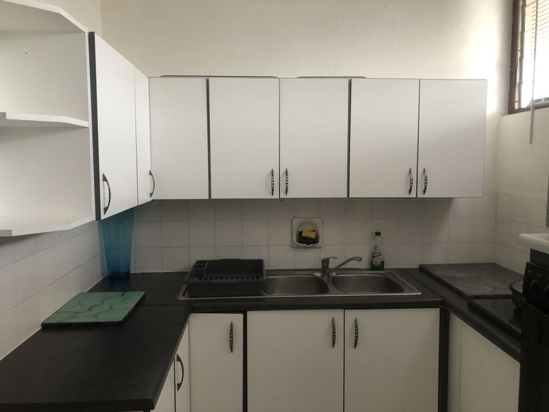 A functional kitchen featuring white built-in cabinetry, dark laminate countertops, and a double bowl stainless steel sink with a tiled splashback.