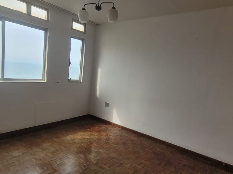 A vacant bedroom featuring parquet flooring, a built-in wardrobe, and large windows offering natural light and ocean views.