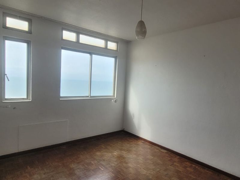 An empty bedroom featuring original parquet flooring, large sliding windows with transom panels, and a neutral interior, offering a blank canvas for renovation.