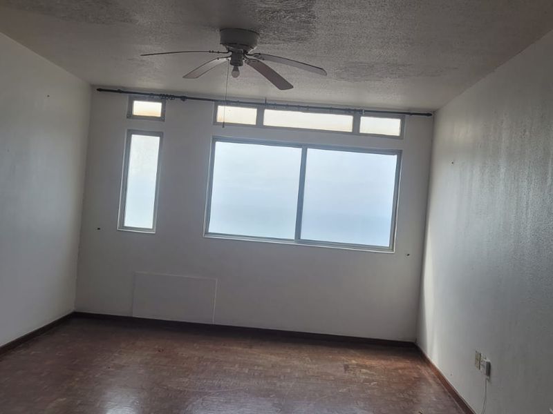 An empty living room featuring a ceiling fan, large sliding windows with natural light, and worn flooring, ready for renovation or staging.