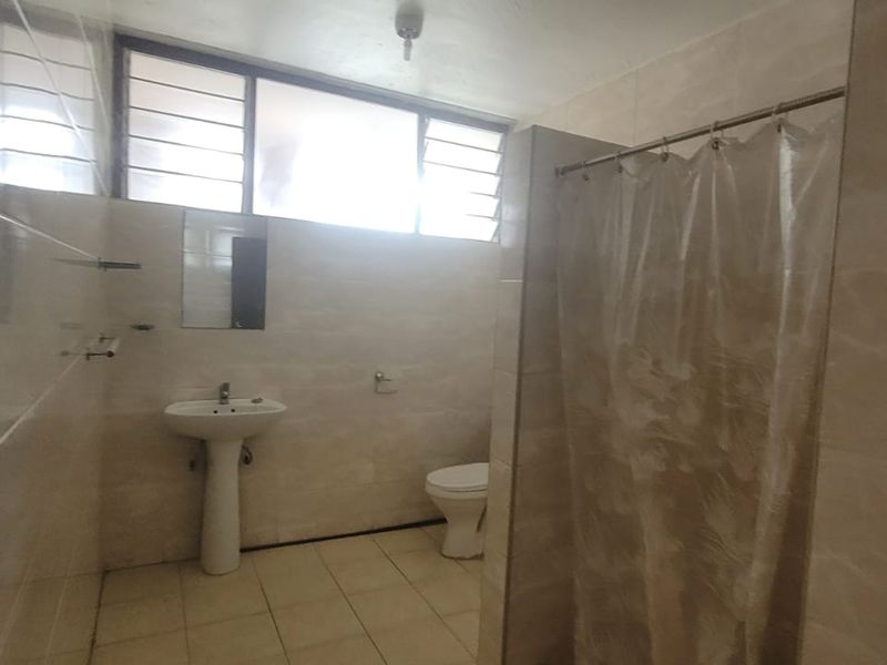 A functional bathroom featuring a pedestal basin, toilet, and shower area with tiled finishes and natural light from louvre windows.