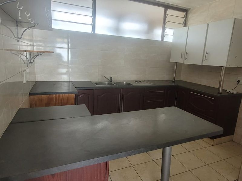 A functional kitchen featuring dark cabinetry, laminate countertops, a double basin sink, and tiled finishes, offering a blank canvas for modern renovation.