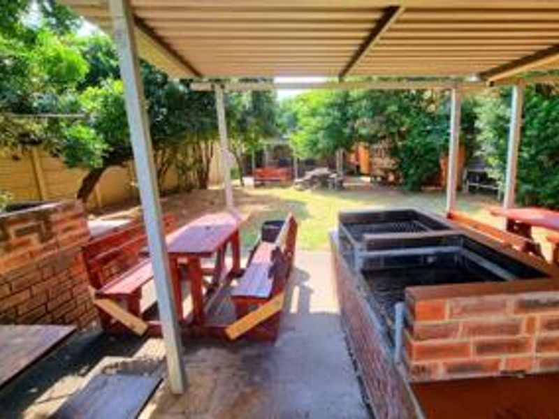 A covered outdoor patio area featuring a built-in brick braai, concrete flooring, and direct access to the garden space.