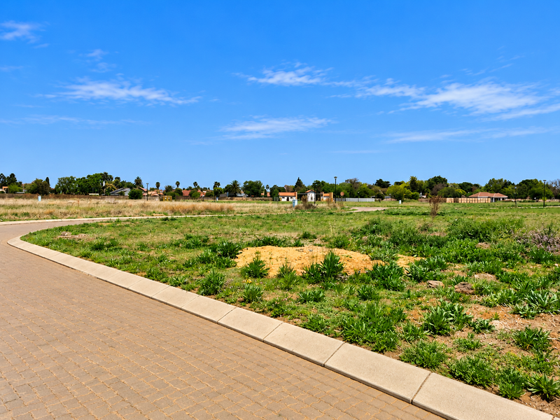 A view of a vacant residential plot featuring a paved driveway and concrete curbing, ready for development.