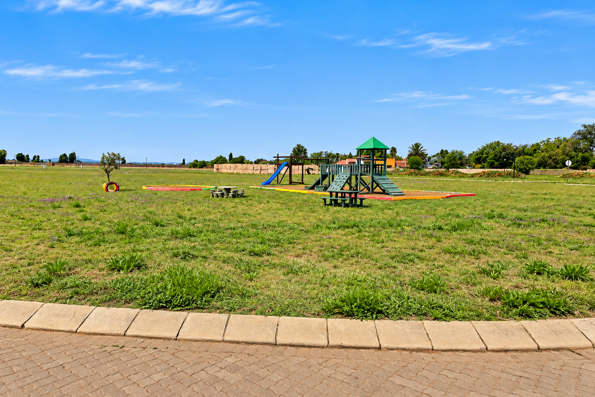 A spacious open residential lot featuring a communal playground area with fixed equipment and paved border detailing.