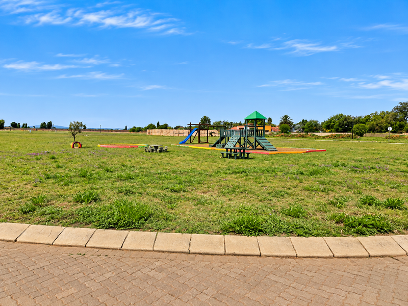 A spacious open residential lot featuring a communal playground area with fixed equipment and paved border detailing.