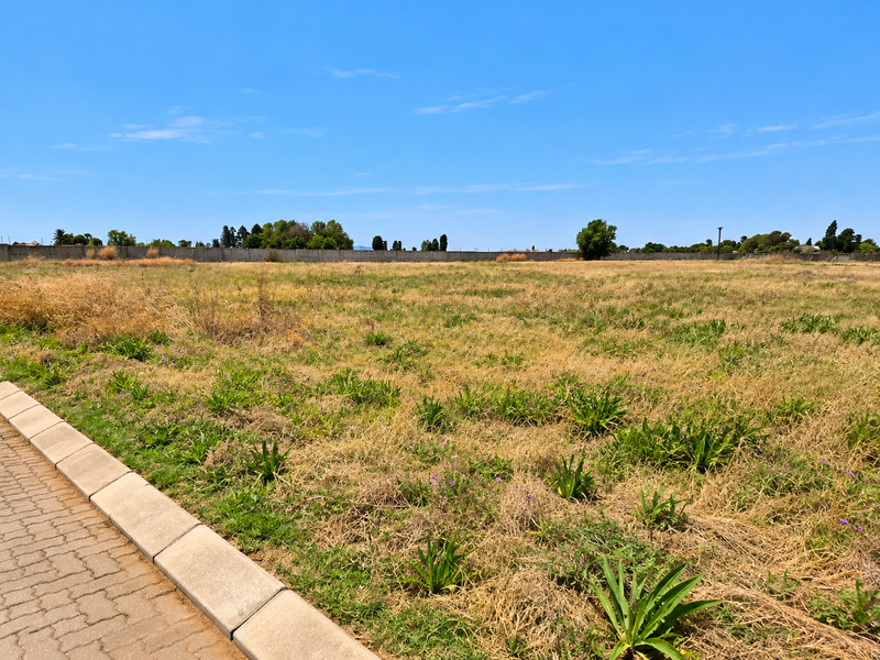 A vacant residential plot featuring a paved curb and perimeter wall, offering a clear, level space ready for development.
