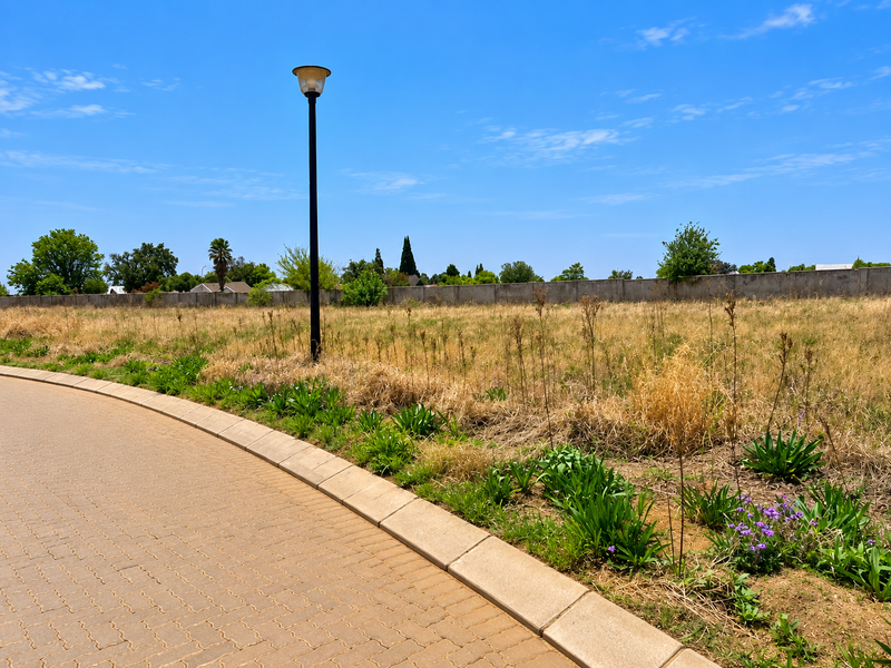 A view of a vacant residential plot featuring a paved driveway, concrete kerbing, a street lamp, and a perimeter wall.