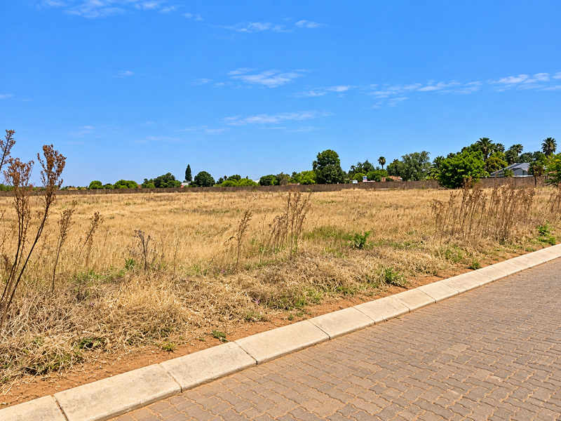 A vacant residential plot featuring a paved curb and boundary wall, offering a clear, level space ready for development.