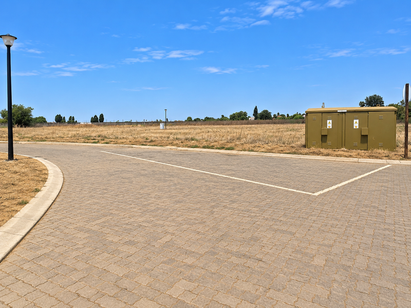 A view of a vacant residential plot featuring a paved driveway, street lighting, and a utility box, ready for development.
