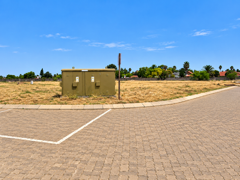 A vacant residential plot featuring a paved driveway, concrete curbing, and an existing electrical utility box on site.