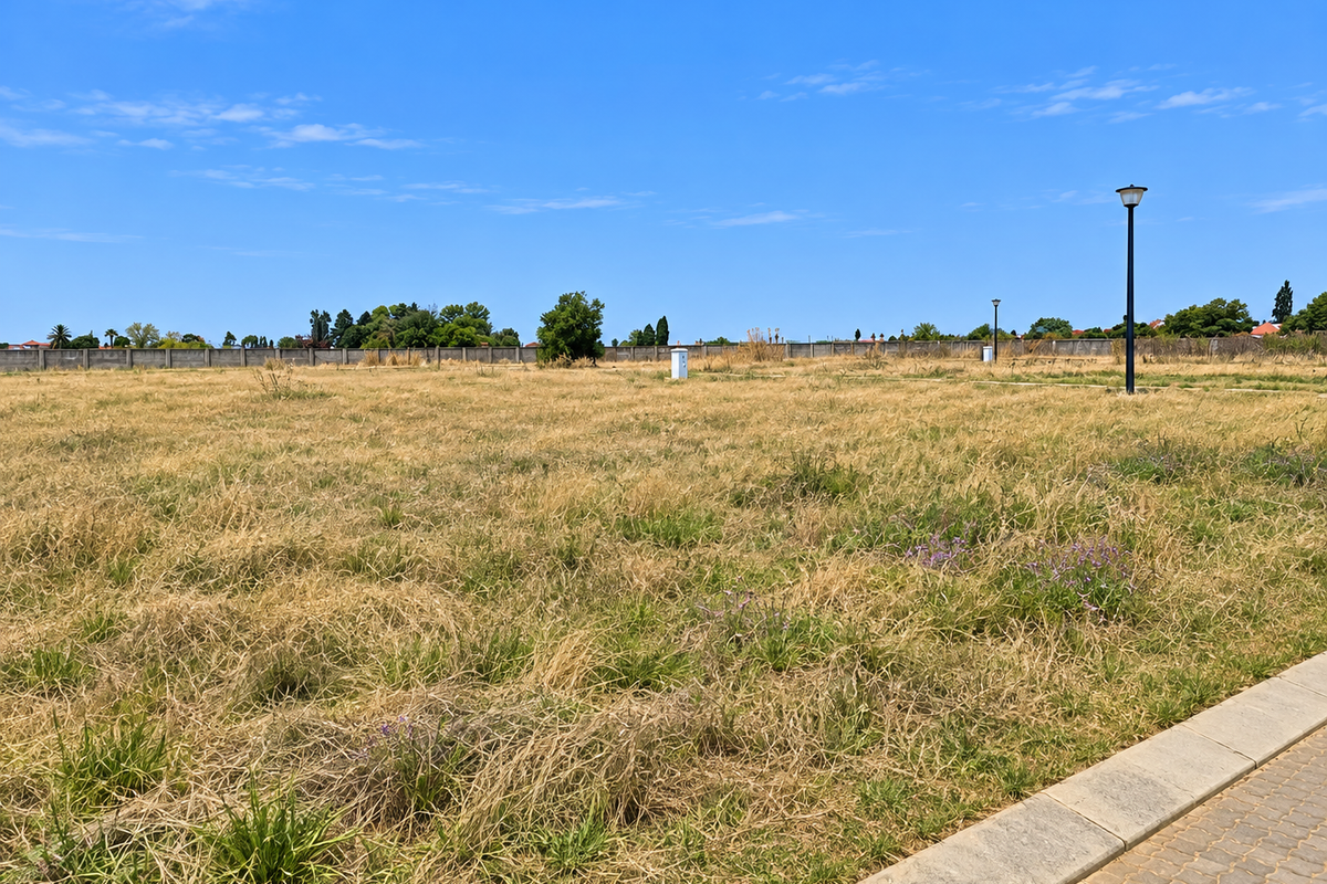 A large, level vacant residential plot featuring dry grass, perimeter walling, and established street lighting, ready for development.