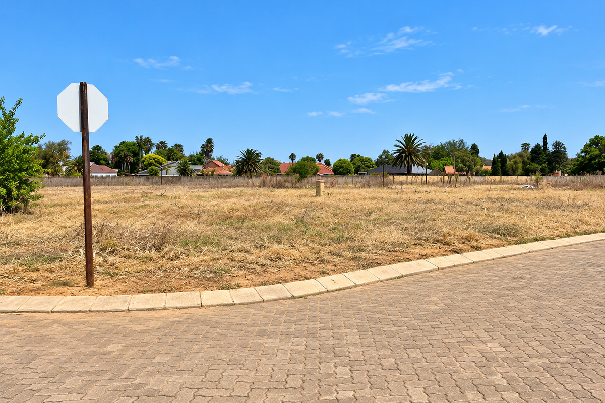 A vacant residential plot featuring a paved street frontage, concrete curbing, and established boundary fencing in a suburban neighborhood setting.