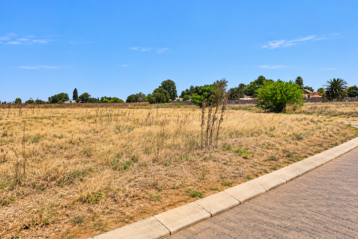 A vacant residential plot featuring dry grass and a paved sidewalk with concrete curbing along the street frontage.