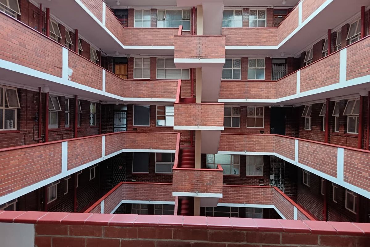 View of the central courtyard and stairwell of a multi-story brick apartment complex with external walkways and security features.