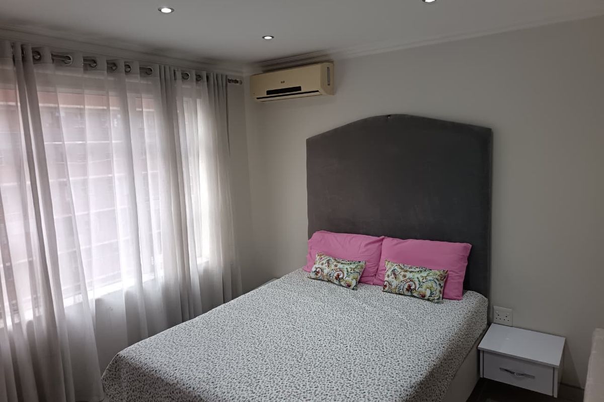 A well-maintained bedroom featuring recessed downlighting, a wall-mounted air conditioning unit, and large windows with security bars.