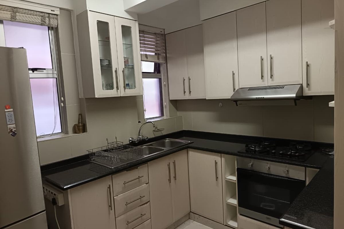 A functional kitchen featuring light-toned cabinetry, dark granite countertops, a built-in oven, gas hob, and an extractor fan.