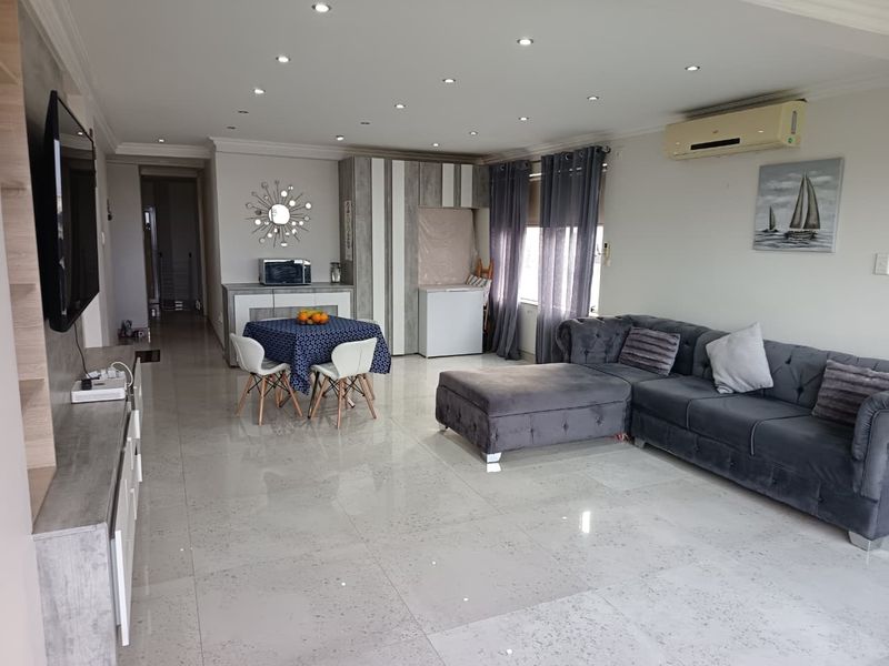 Spacious open-plan living area featuring polished porcelain floor tiles, recessed downlighting, and a wall-mounted air conditioning unit.