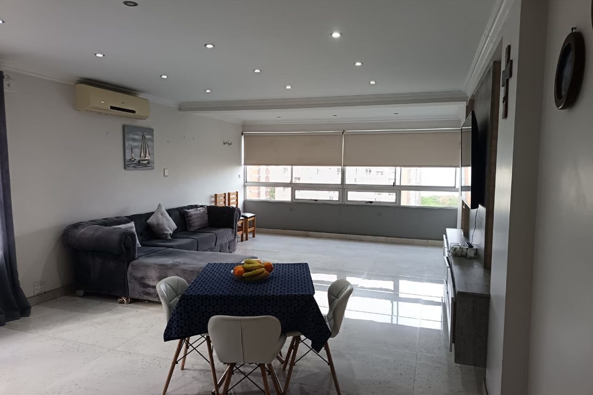 Spacious open-plan living area featuring tiled flooring, recessed downlighting, and a wall-mounted air conditioning unit with large windows providing natural light.