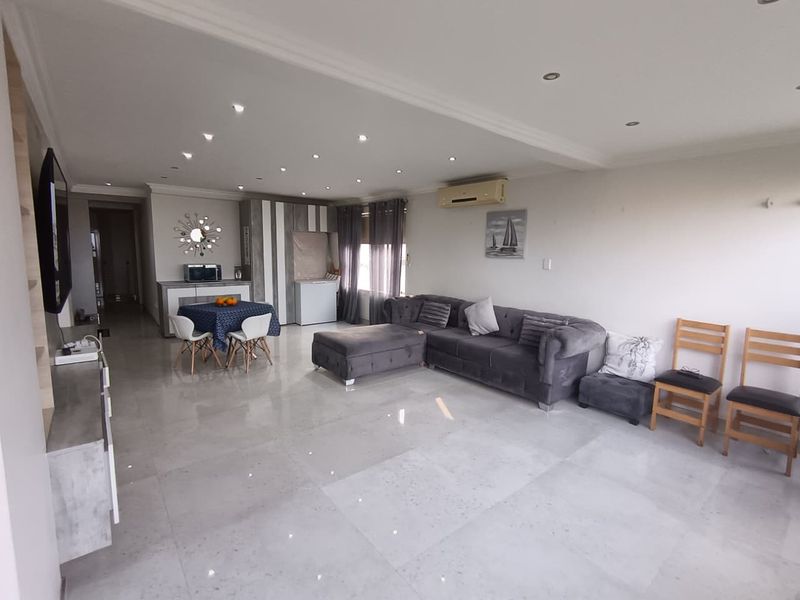 Spacious open-plan living area featuring polished porcelain floor tiles, recessed downlighting, and a wall-mounted air conditioning unit.