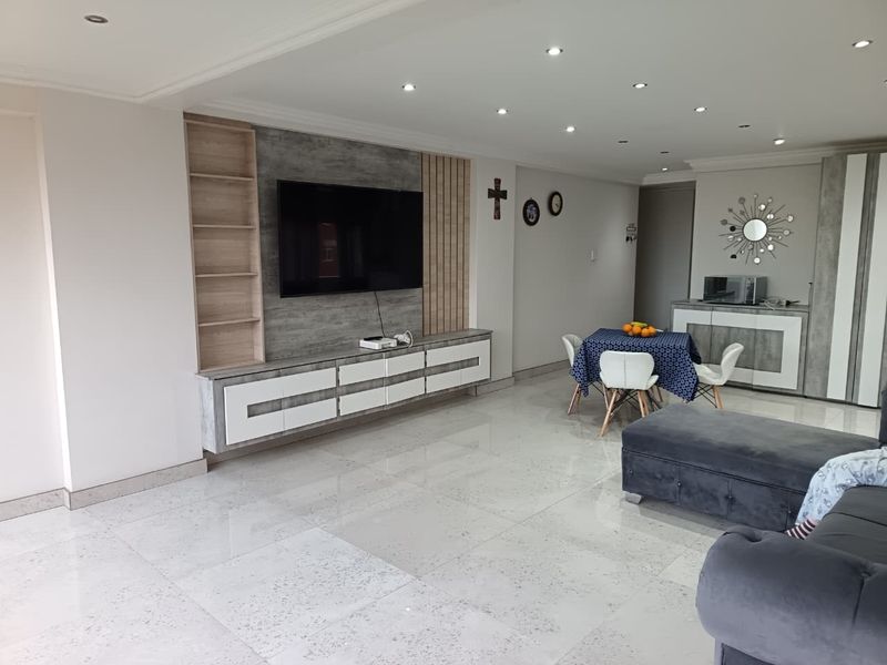 Spacious open-plan living and dining area featuring modern porcelain floor tiles, recessed downlighting, and a custom built-in media wall with integrated cabinetry.