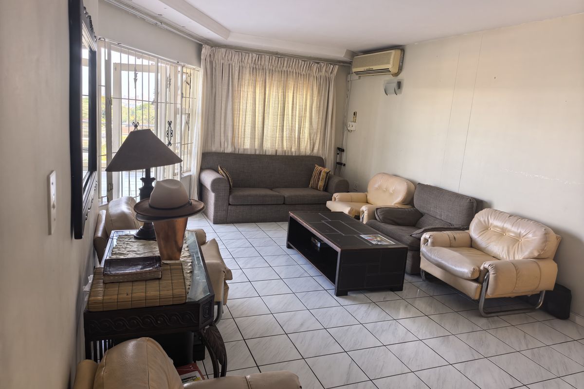 Spacious living room featuring tiled flooring, a wall-mounted air conditioning unit, and large windows with security gates.