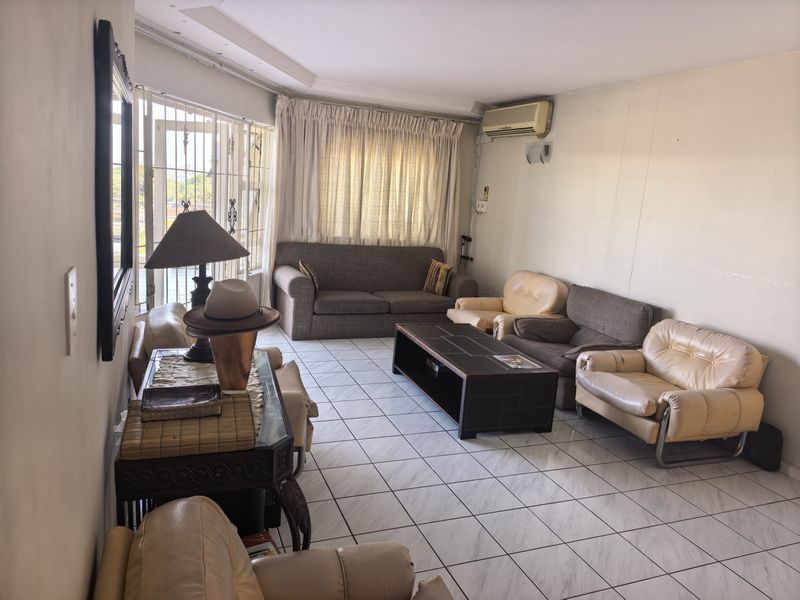 Spacious living room featuring tiled flooring, a wall-mounted air conditioning unit, and large windows with security gates.
