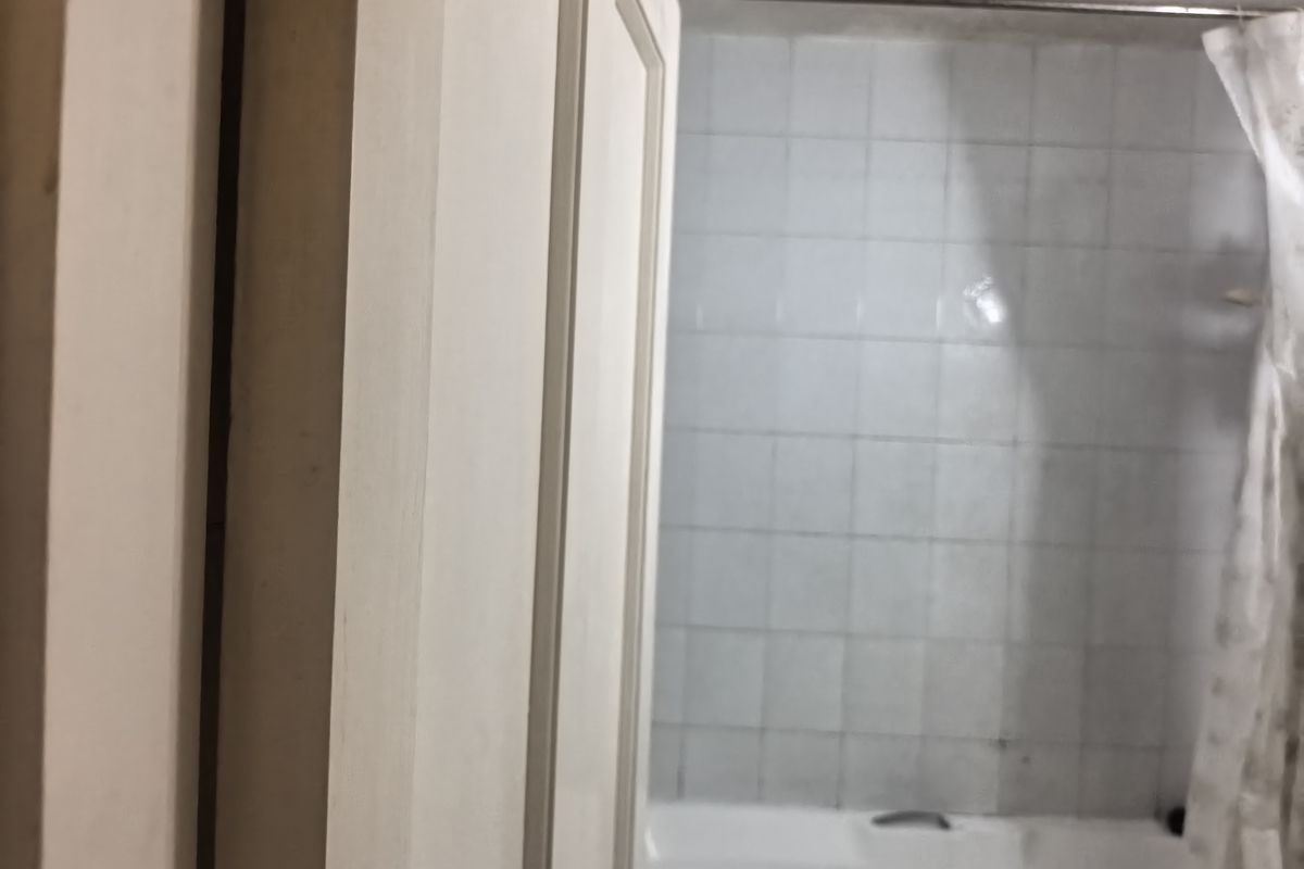 A view into a bathroom featuring a bathtub with wall tiling and a shower curtain rail, requiring cosmetic updates.