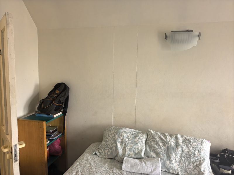 A bedroom featuring a wall-mounted light fixture and standard internal door, showing signs of wear on the wall surfaces.
